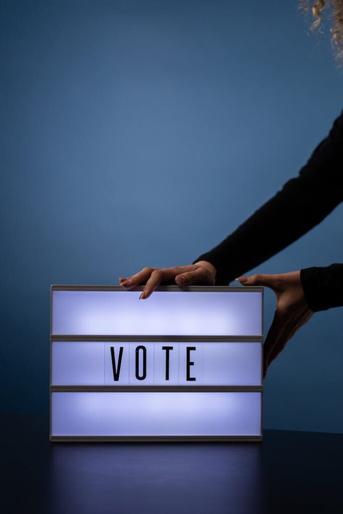 Close-up of hands placing a lit vote sign with a bold message on a blue background.